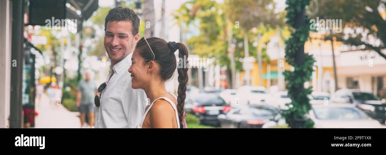 Glückliches interrassisches Paar, das auf der Straße der Stadt mit dem Bannerpanorama spazierengeht Der junge Mann und die asiatische Frau blicken zusammen auf das Schaufenster des Ladens, Neapel Stockfoto