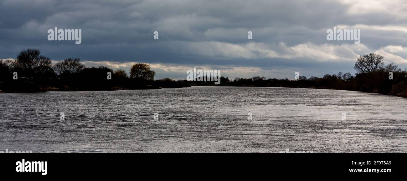 Dunkle Silhouette eines Flussufers mit großen grauen Wolken Und einige Sonnenstrahlen, die durchziehen Stockfoto