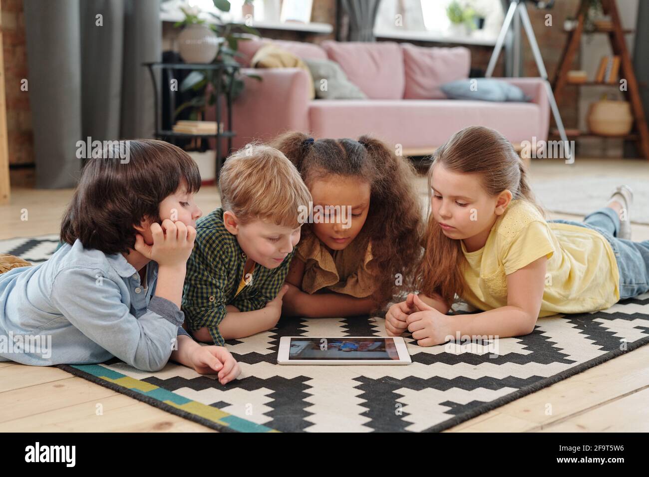 Eine Gruppe von Kindern, die auf dem Boden liegen und sich Cartoons ansehen Gemeinsam auf einem digitalen Tablet zu Hause Stockfoto