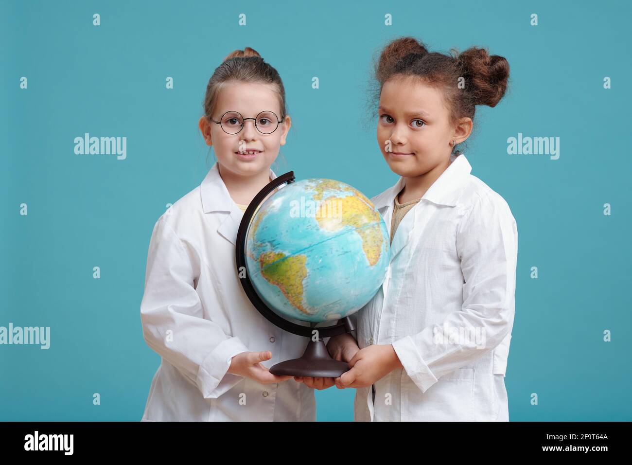 Portrait von zwei kleinen Mädchen halten große Welt Globus und Lächelnd vor blauem Hintergrund auf die Kamera Stockfoto