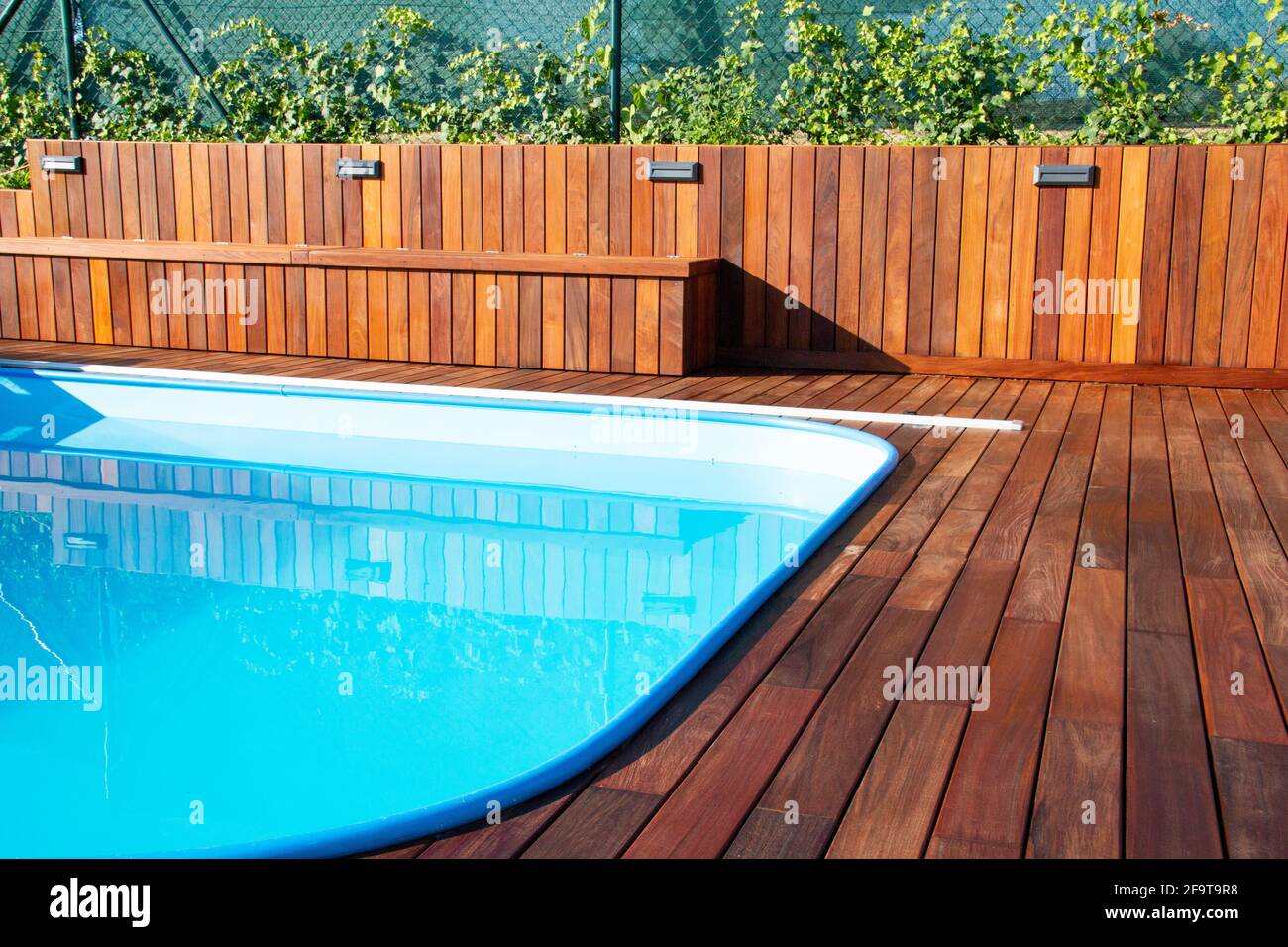 IPE Holzterrasse und Swimmingpool. Hinterhof-Terrasse am Pool, blaues Wasser im Kontrast zu tropischen Hartholzbrettern und wunderschöner Holzstruktur Stockfoto