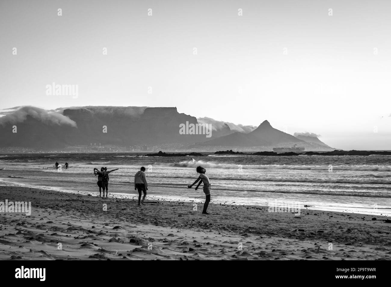 Zwei afrikanische Frauen, die bei Sonnenuntergang am Strand spazieren, mit Tafelberg und Kapstadt im Hintergrund, Milnerton Beach, Kapstadt, Südafrika Stockfoto