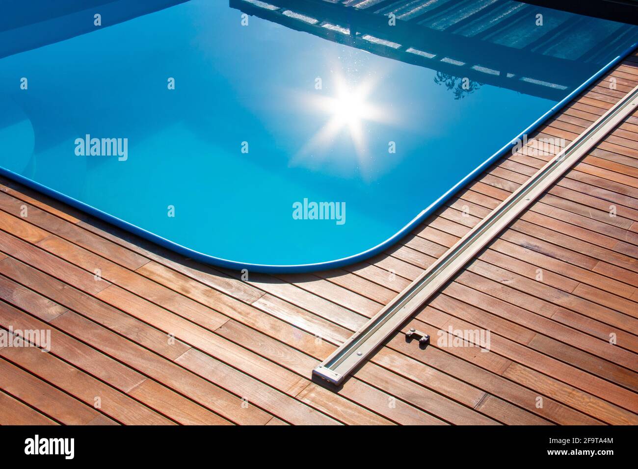 IPE Holzterrasse um den Pool, Rand des Outdoor Swimmingpools mit Sonnenreflexion auf dem blauen Wasser, tropische Holzterrasse aus nächster Nähe Stockfoto