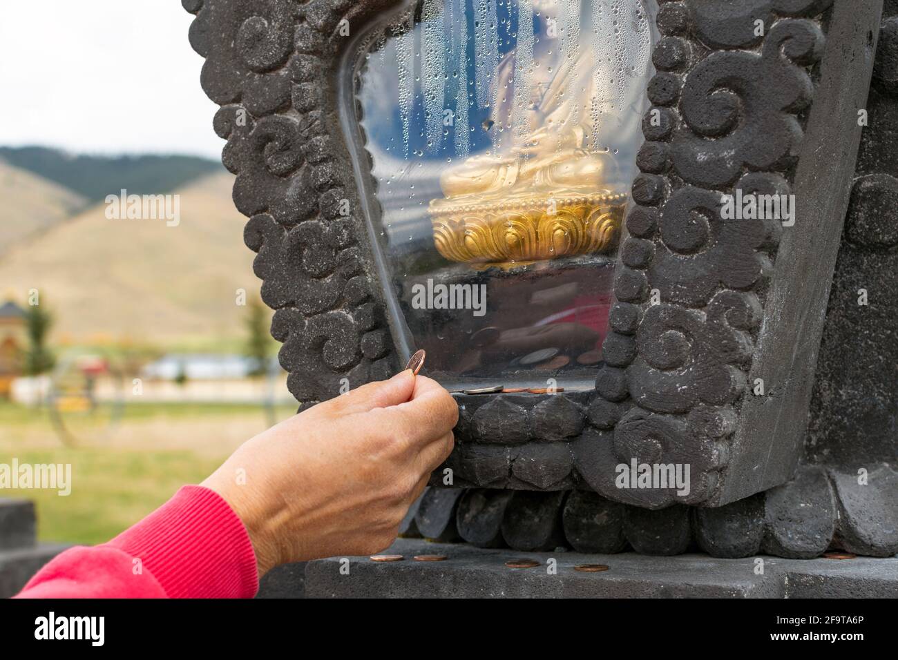 Ein Besucher platziert eine Münze in der Nähe einer umschlossenen goldenen Buddha-Statue, um Glück zu haben, im Garten der tausend Buddhas in Arlee, Montana, USA Stockfoto