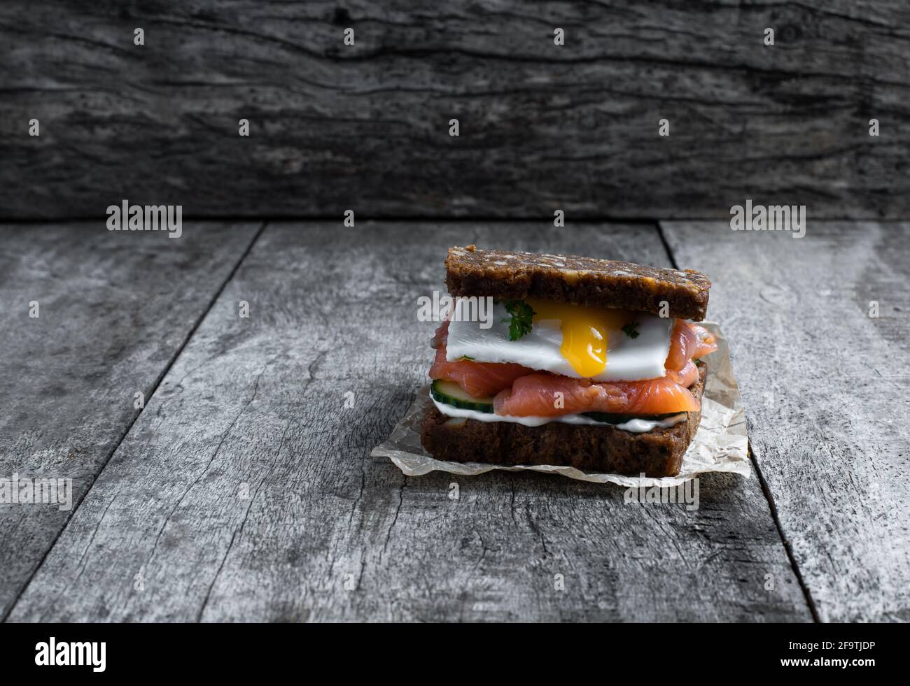 Gesundes Sandwich mit geräuchertem Lachs und Spiegelei auf rustikalem Holztisch Stockfoto