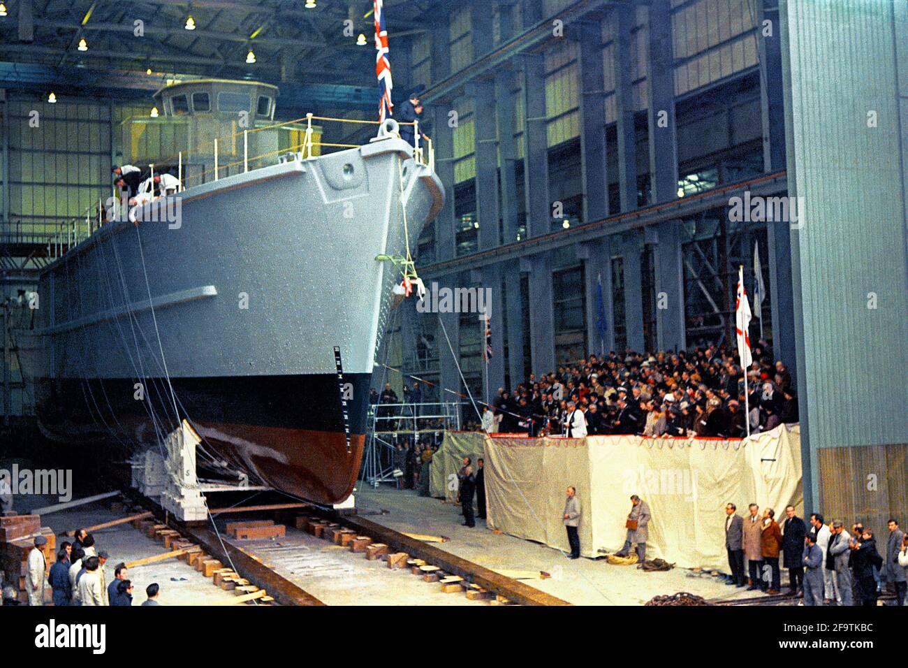 AJAXNETPHOTO. JANUAR 1972. WOOLSTON, ENGLAND. - DAS ERSTE PLASTIKSCHIFF DER WELT - HMS WILTON, EIN MINENJÄGER DER ROYAL NAVY NACH DEM DESIGN DER TONNER-KLASSE, WAR DAS ERSTE KRIEGSSCHIFF DER WELT, DAS VON VOSPER THORNYCROFT IN SEINEM WERK IN WOOLSTON AUS GLASFASER GEBAUT WURDE. DIE ERÖFFNUNGSZEREMONIE IST AUF DIESEM FOTO IM GANGE. FOTO: JONATHAN EASTLAND/AJAX. REF:544160 1 11 Stockfoto