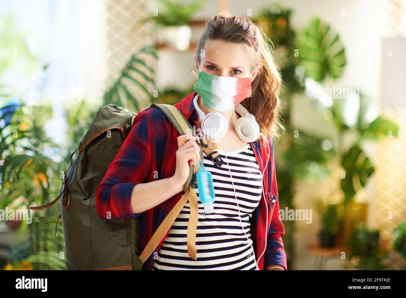 Reisen während der Covid-19-Pandemie. Porträt einer Reisenden Frau mittleren Alters mit medizinischer Maske, Rucksack, Desinfektionsmittel und Kopfhörern in der Mod Stockfoto