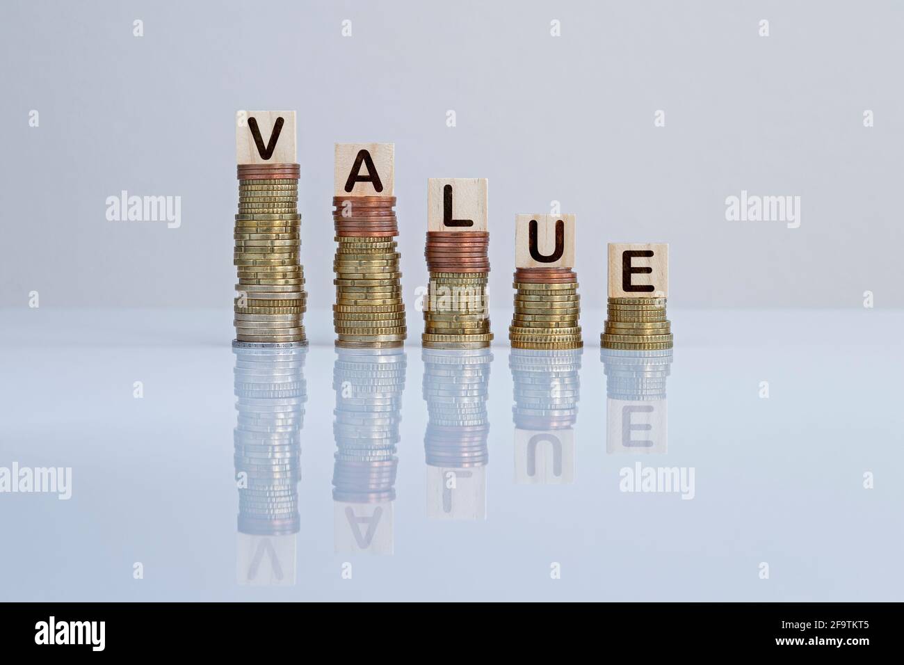 Wort „WERT“ auf Holzblöcken auf absteigenden Münzstapeln vor grauem Hintergrund. Konzeptfoto von Geschäft, Finanzen und Scheitern. Stockfoto