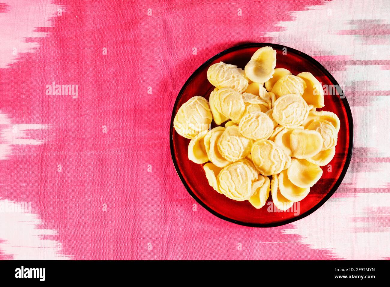 Orecchiette Pasta in roter Schüssel auf farbigem Tuch, eine kleine Ohrenförmige Pasta mit der Mitte dünner als der Rand Und eine raue Oberfläche Stockfoto