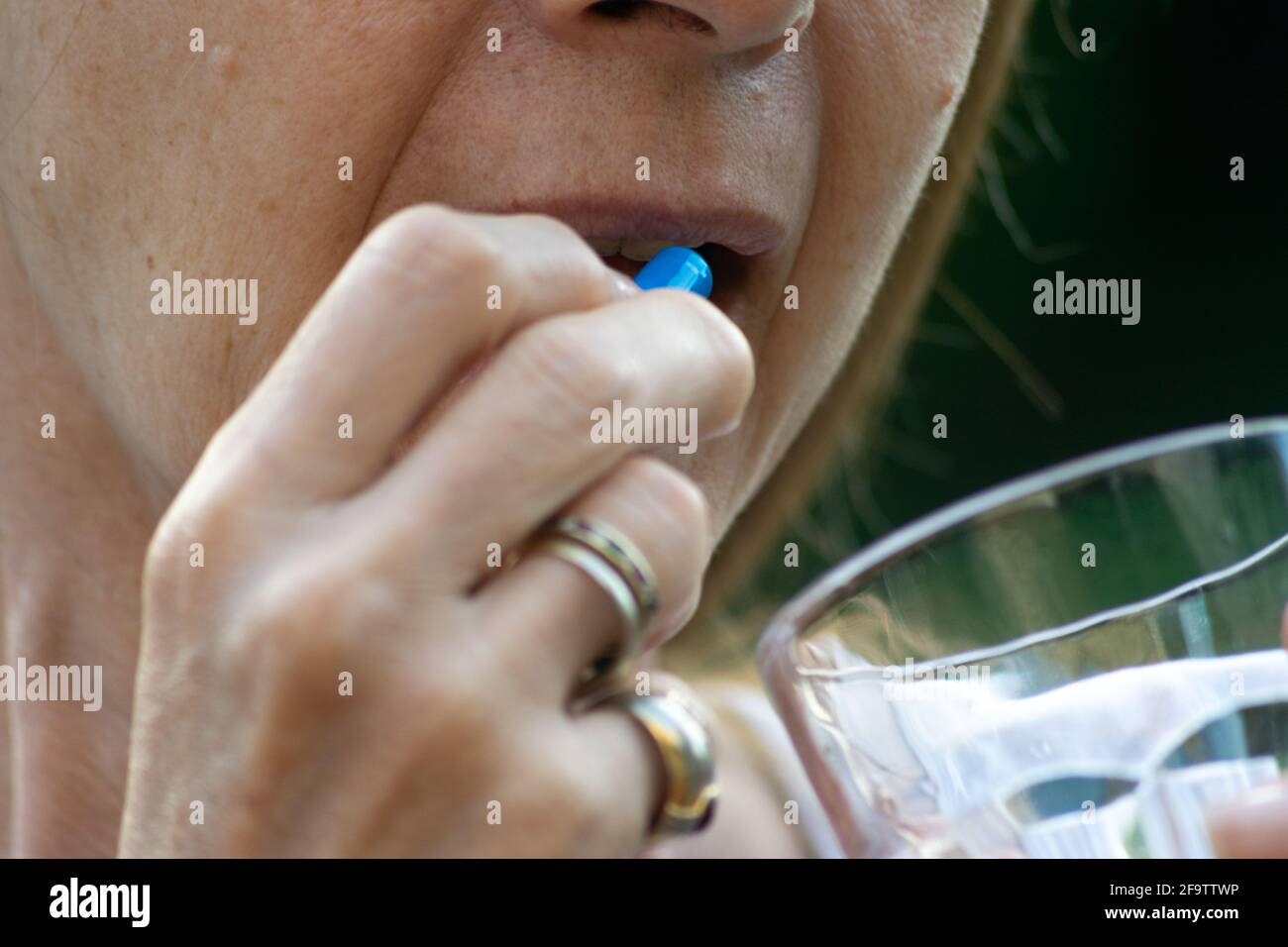 Person, die ein blaues Medikament mit einem Glas einnehme Wasser Stockfoto