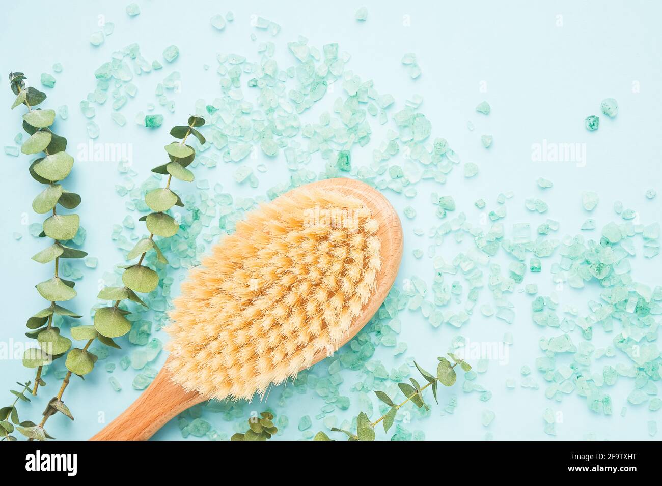 SPA-Behandlungskonzept. Anti-Cellulite-Körperbürste, Eukalyptuszweige und Badesalz auf blauem Hintergrund. Draufsicht, Platz für Text kopieren Stockfoto