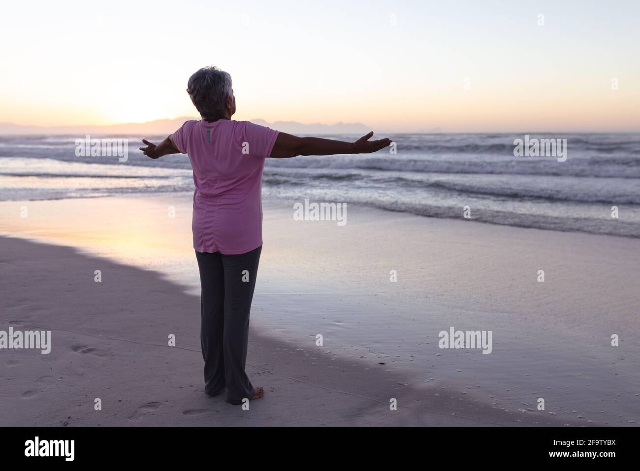 Rückansicht einer älteren afroamerikanischen Frau, die mit ihr stand Die Arme sind am Strand weit geöffnet Stockfoto
