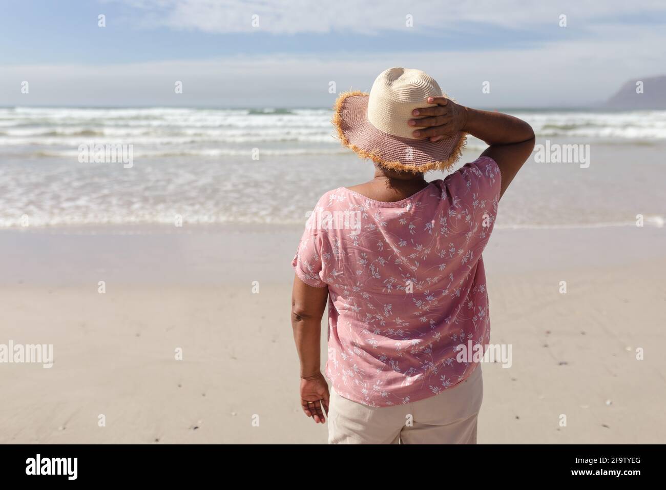 Rückansicht einer älteren afroamerikanischen Frau, die auf dem stand Strand Stockfoto