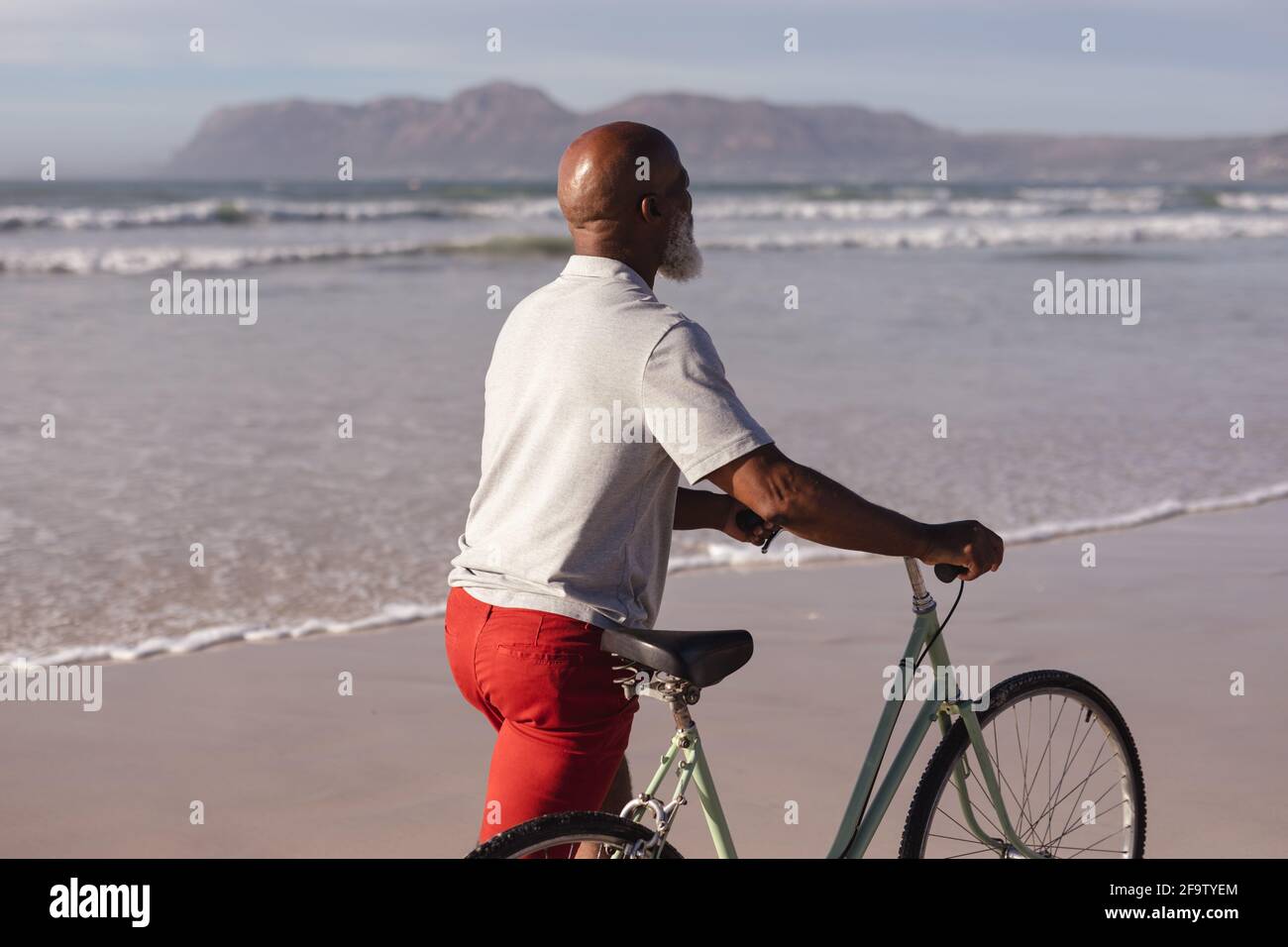 Älterer afroamerikanischer Mann mit Fahrrad, der zusammen auf dem läuft Strand Stockfoto