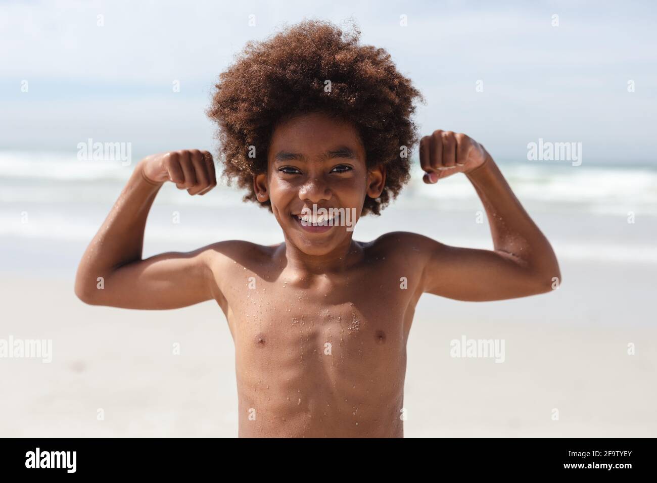Porträt eines afroamerikanischen Jungen, der seinen Bizeps an der biegt Strand Stockfoto