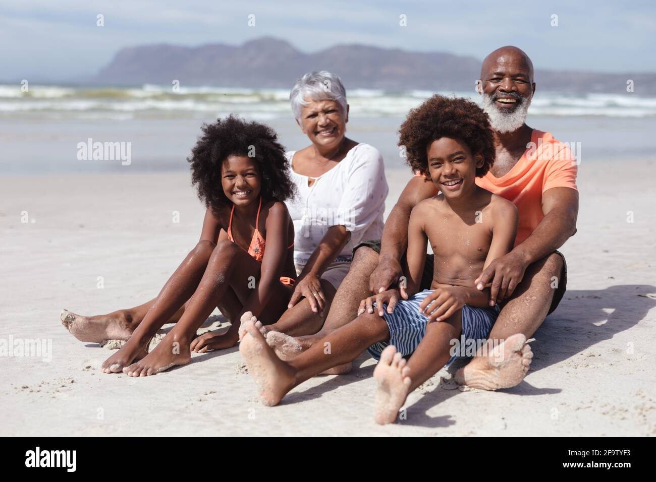 Porträt afroamerikanischer Großeltern und Enkelkinder, die lächeln, während sie sitzen Am Strand Stockfoto