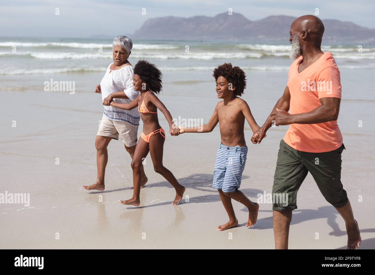afroamerikanische Großeltern und Enkelkinder, die die Hände am Fuß halten Strand Stockfoto
