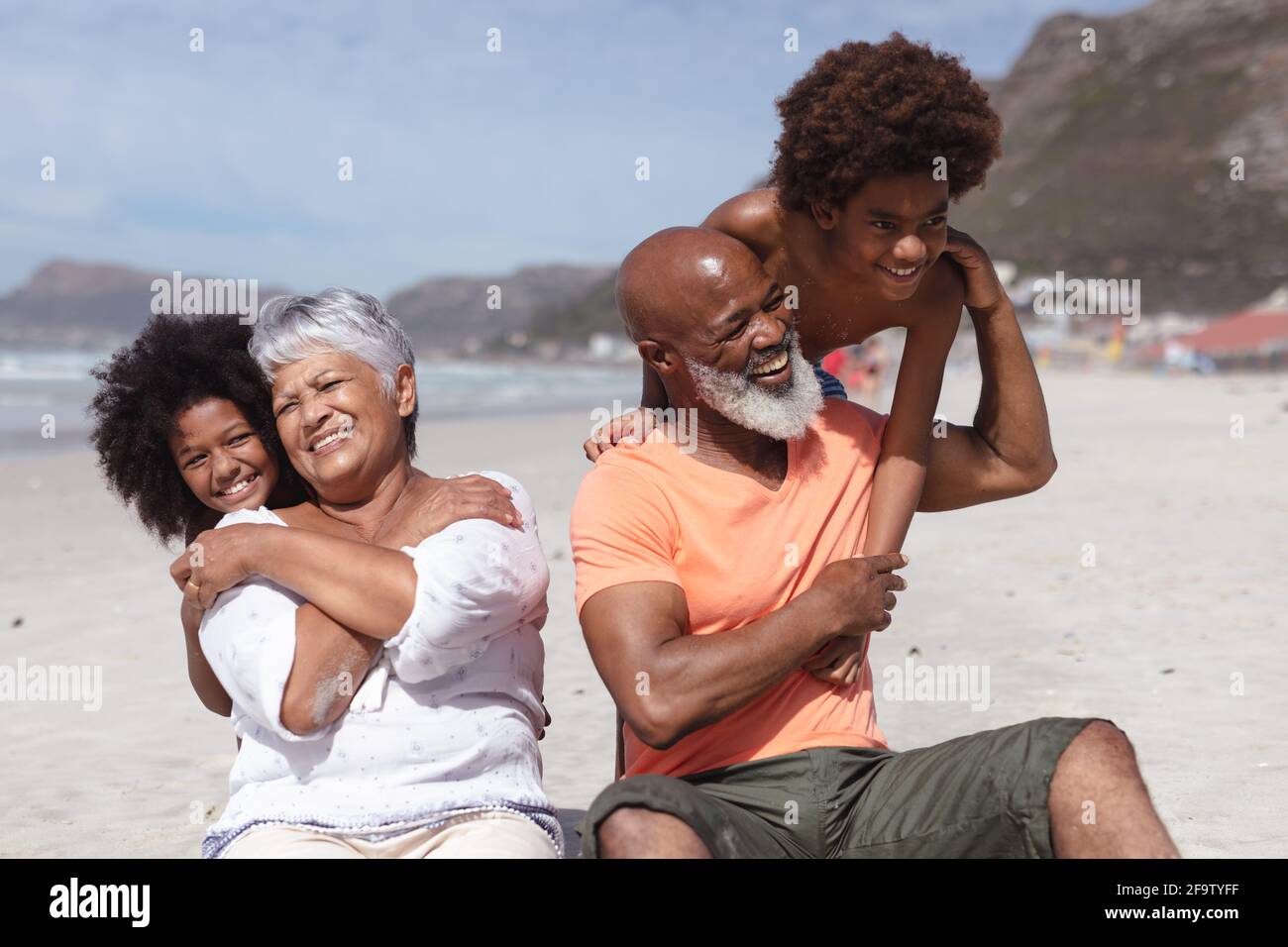 afroamerikanische Großeltern und Enkelkinder umarmen sich, während sie auf dem sitzen Strand Stockfoto