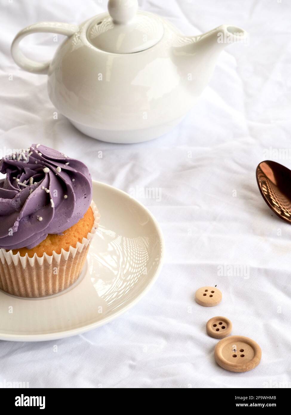 Cupcake mit violetter Glasur und weißer Teekannen auf einem weißen Strukturierter Hintergrund Stockfoto