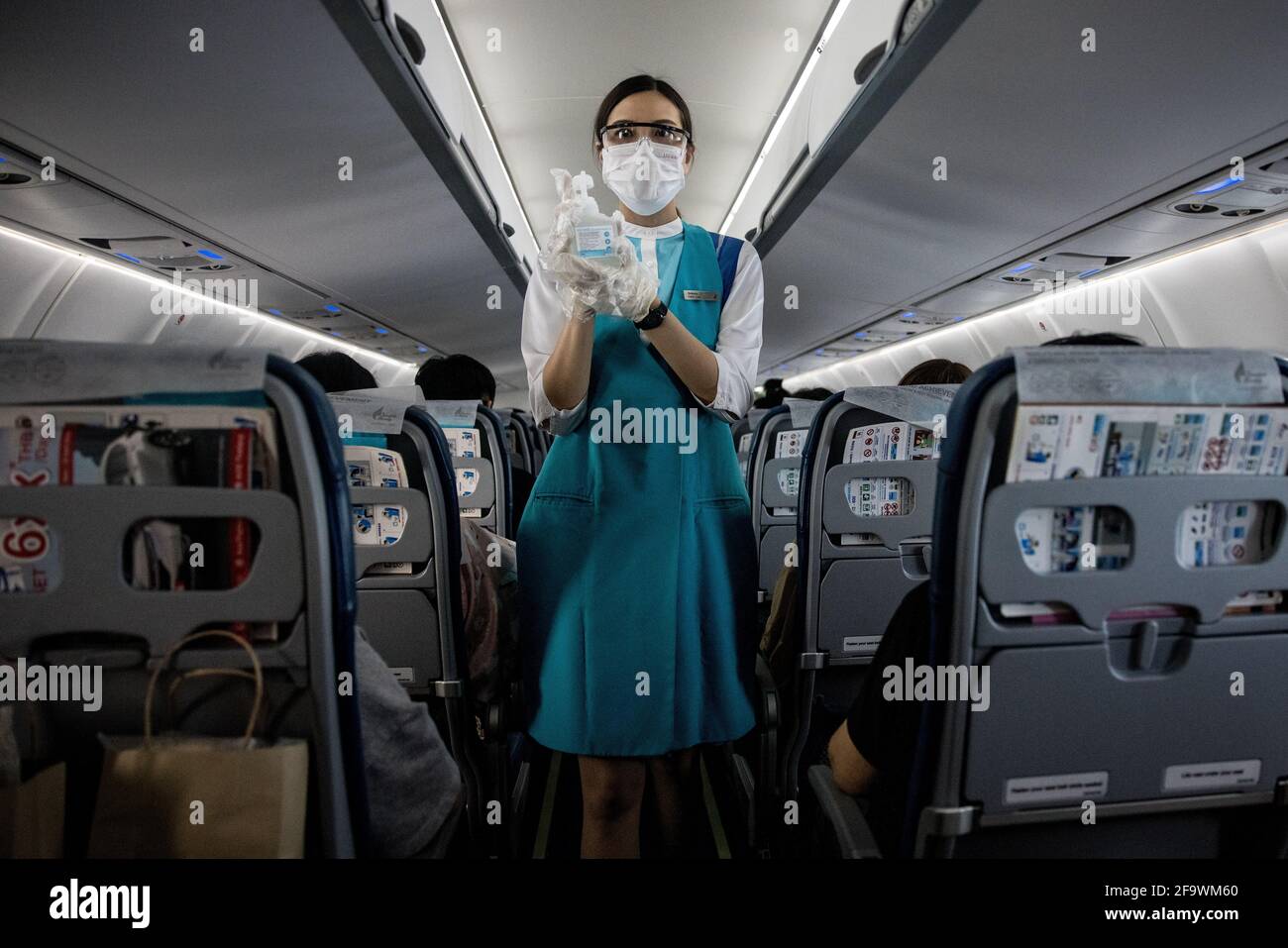 Ein Mitglied der Kabinencrew von Bangkok Airways, das eine Gesichtsmaske und eine Schutzbrille trägt, bietet Passagieren an Bord eines Fluges vom Flughafen Bangkok Suvarnabhumi nach Koh Samui, Thailand, am 8. März 2021 während der globalen Covid-19-Pandemie ein Händedesinfektionsmittel an. Stockfoto