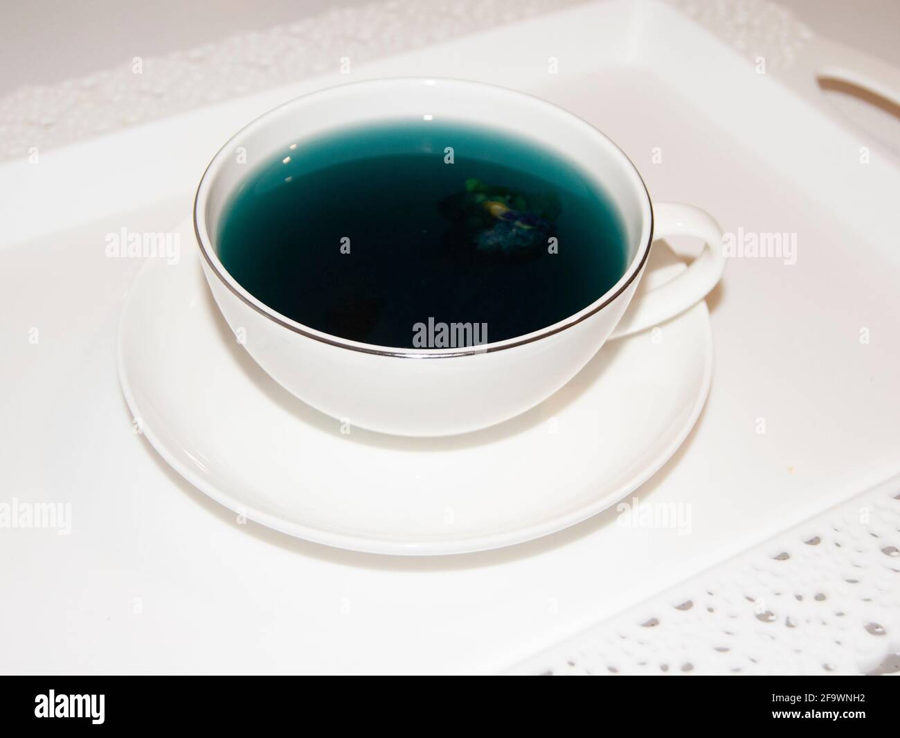 Die Stimmungsfarbe ist blau - blauer Tee in einem weißen Becher, der auf einer weißen Untertasse und einem weißen Tablett steht. Nützliche Getränke, heilende Eigenschaften. Phytotherapie. Te Stockfoto