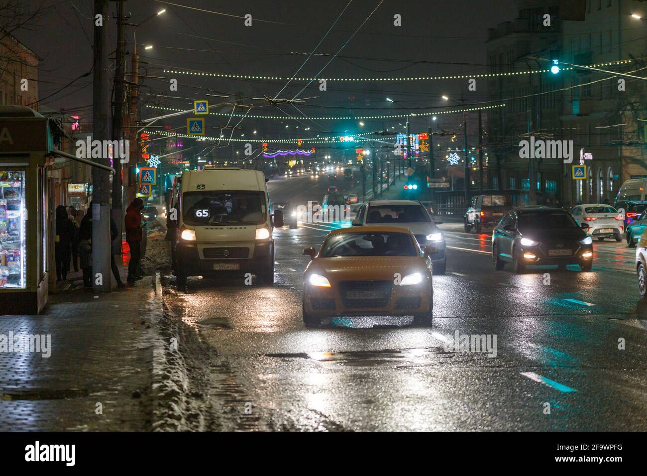 Tula, Russland - 20. Dezember 2020: Nächtlicher Autoverkehr auf einer breiten Stadtstraße und Einsteigen von Passagieren in ein Taxi mit fester Route. Stockfoto