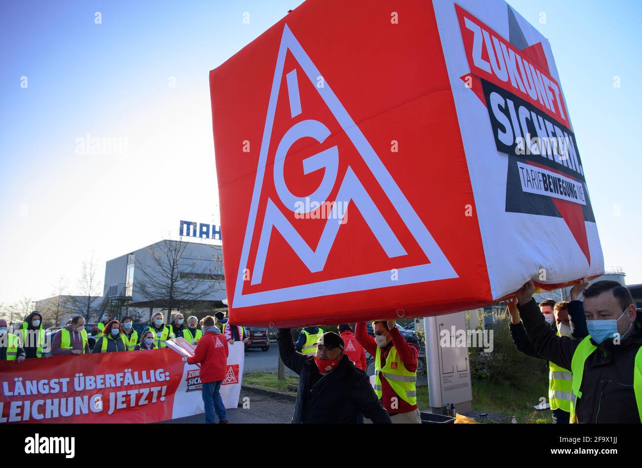 Wustermark, Deutschland. April 2021. Mitarbeiter der Frühschicht der Mahle Filtersysteme GmbH und Vertreter der IG Metall führen einen luftgefüllten Würfel mit der Aufschrift „die Zukunft sichern!“ An den Eingang des Unternehmens heute Morgen während eines Warnstreiks der IG Metall. Die Aktion, die sich über drei Schichten erstreckte, sollte unter anderem die Forderungen nach einer Lohnerhöhung und zukünftigen Tarifverträgen betonen. Quelle: Soeren Stache/dpa-Zentralbild/ZB/dpa/Alamy Live News Stockfoto