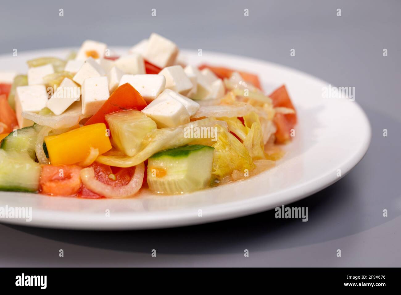 Griechischer Salat auf weißem Teller auf grauem Hintergrund. Stockfoto