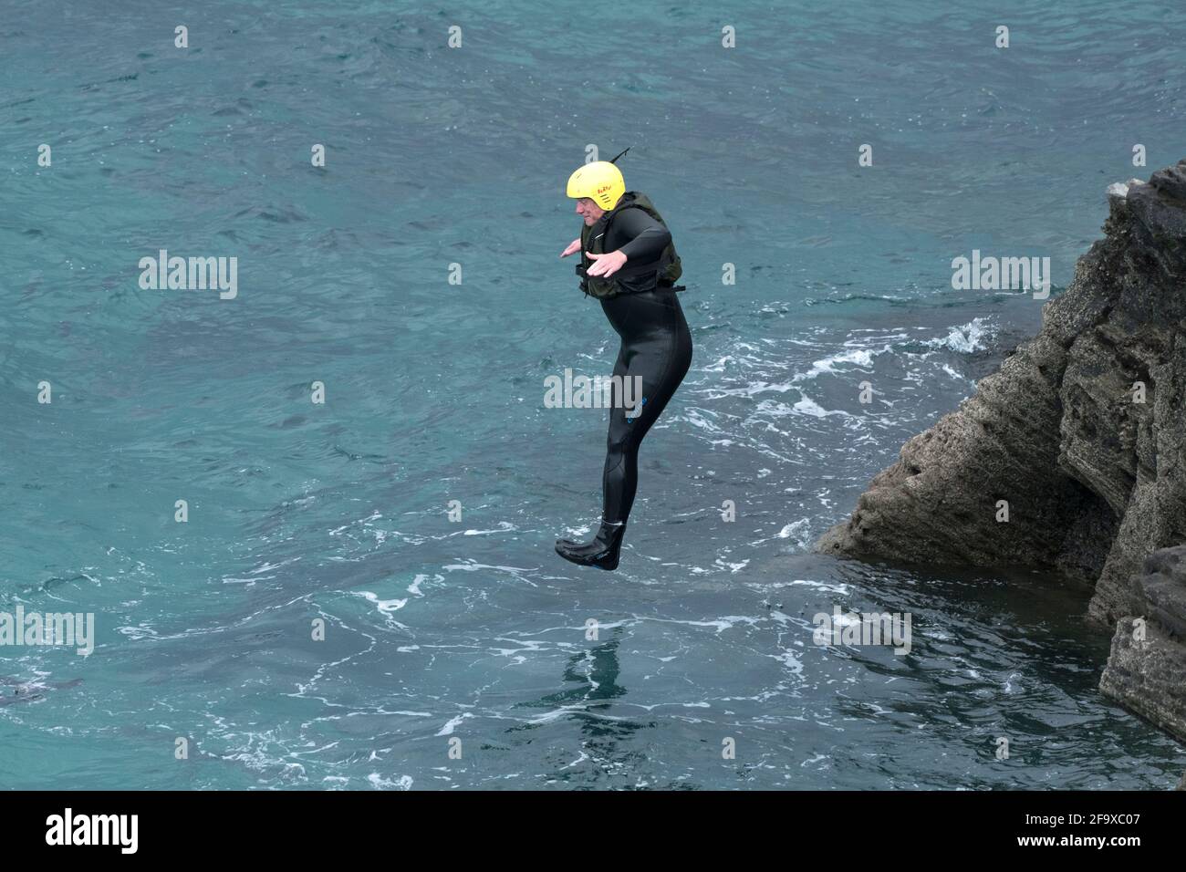 Ein koaSteering Urlauber, der von Felsen ins Meer springt, auf einer koaSteering Reise um Towan Head in Newquay in Cornwall. Stockfoto