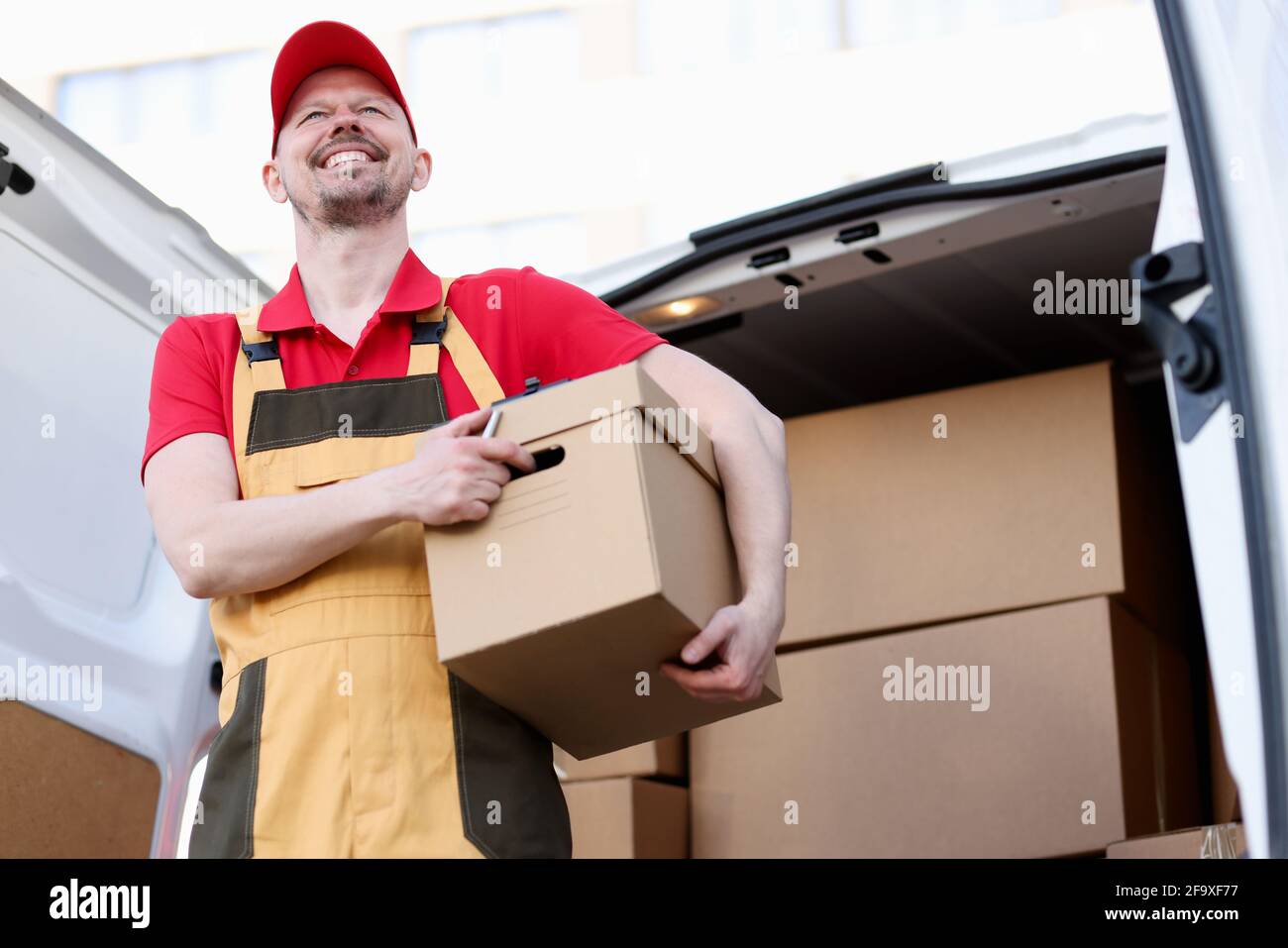 Lächelnder männlicher Kurier mit großem Karton Stockfoto
