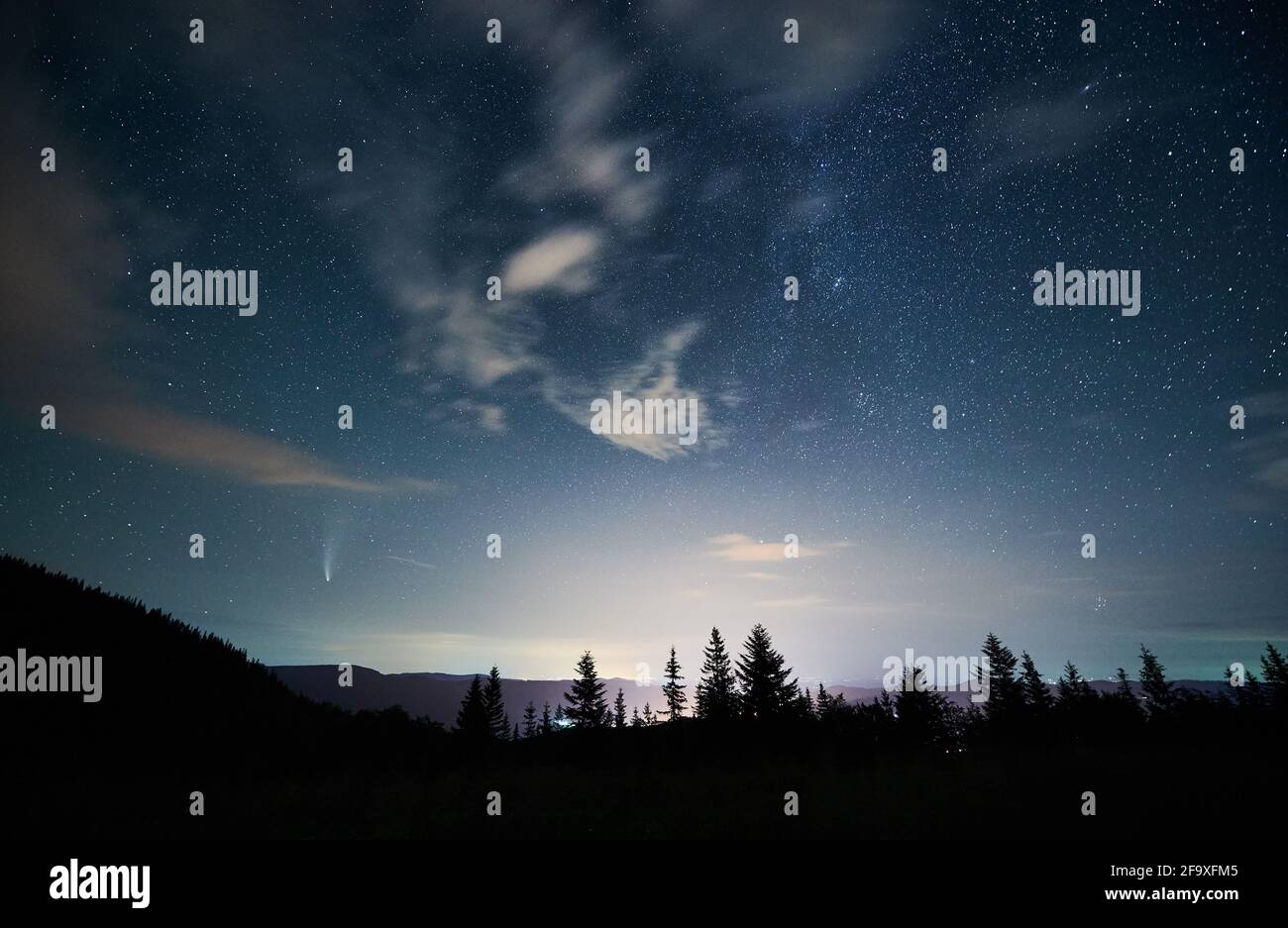 Herrlicher Blick auf den nächtlichen Sternenhimmel über Nadelwald in den Bergen. Landschaft von Bergwald mit Nadelbäumen unter blauem Himmel mit Sternen und Komet Neowise. Konzept der Astronomie und Galaxie. Stockfoto