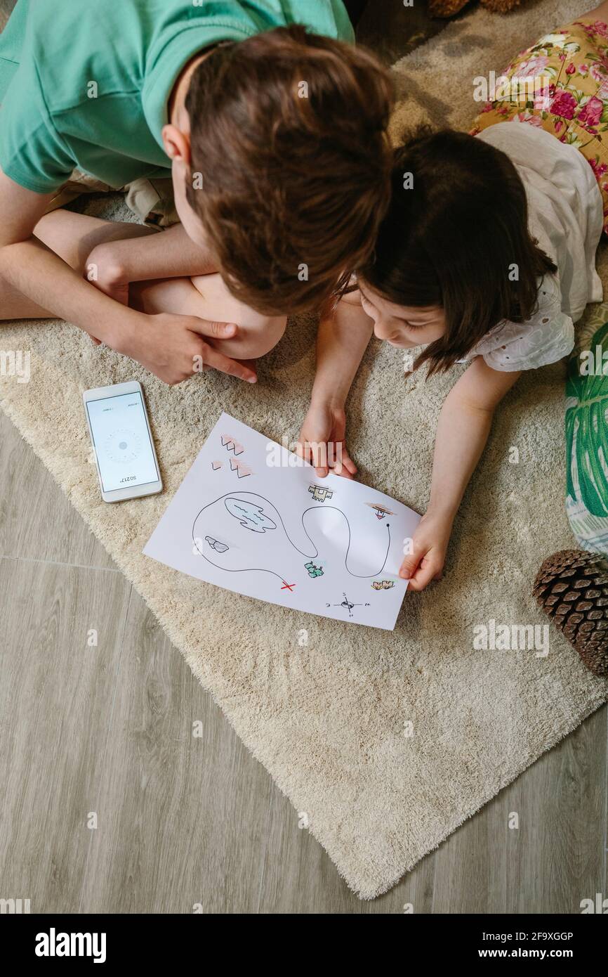 Draufsicht auf Kinder, die zu Hause auf Schatzsuche spielen Der Teppich Stockfoto