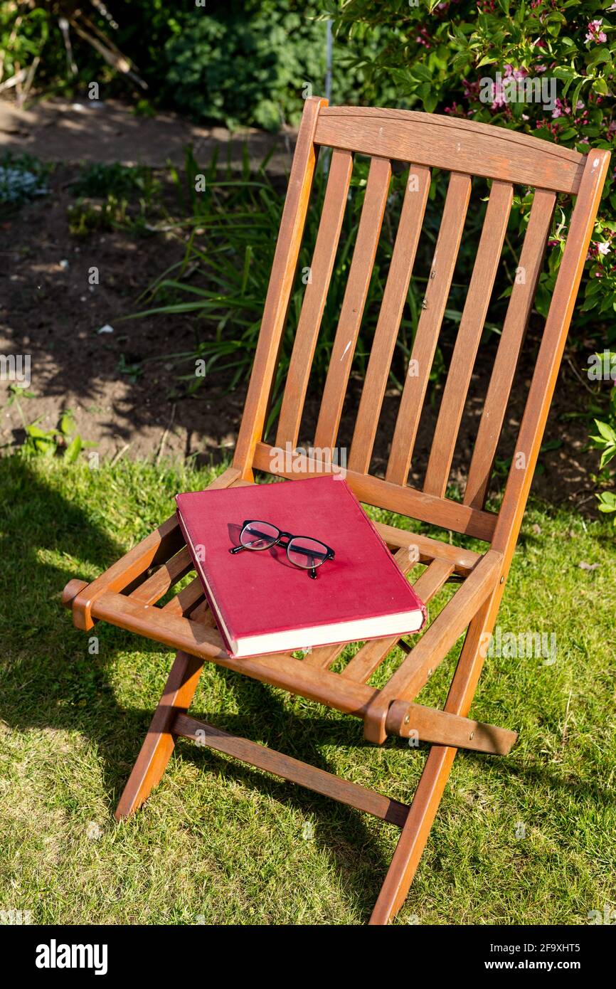 Ein großes Hardcover-Buch, das auf einem Stuhl mit einer Lesebrille auf dem Stuhl aufliegt. Lesen im Freien Konzept Stockfoto