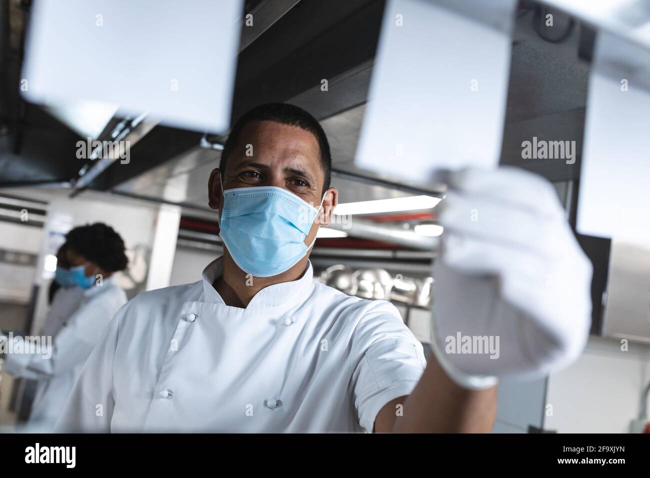 Gemischter Profi-Koch mit Hygienehandschuhen, der Bestellungen ansieht Und Gesichtsmaske Stockfoto