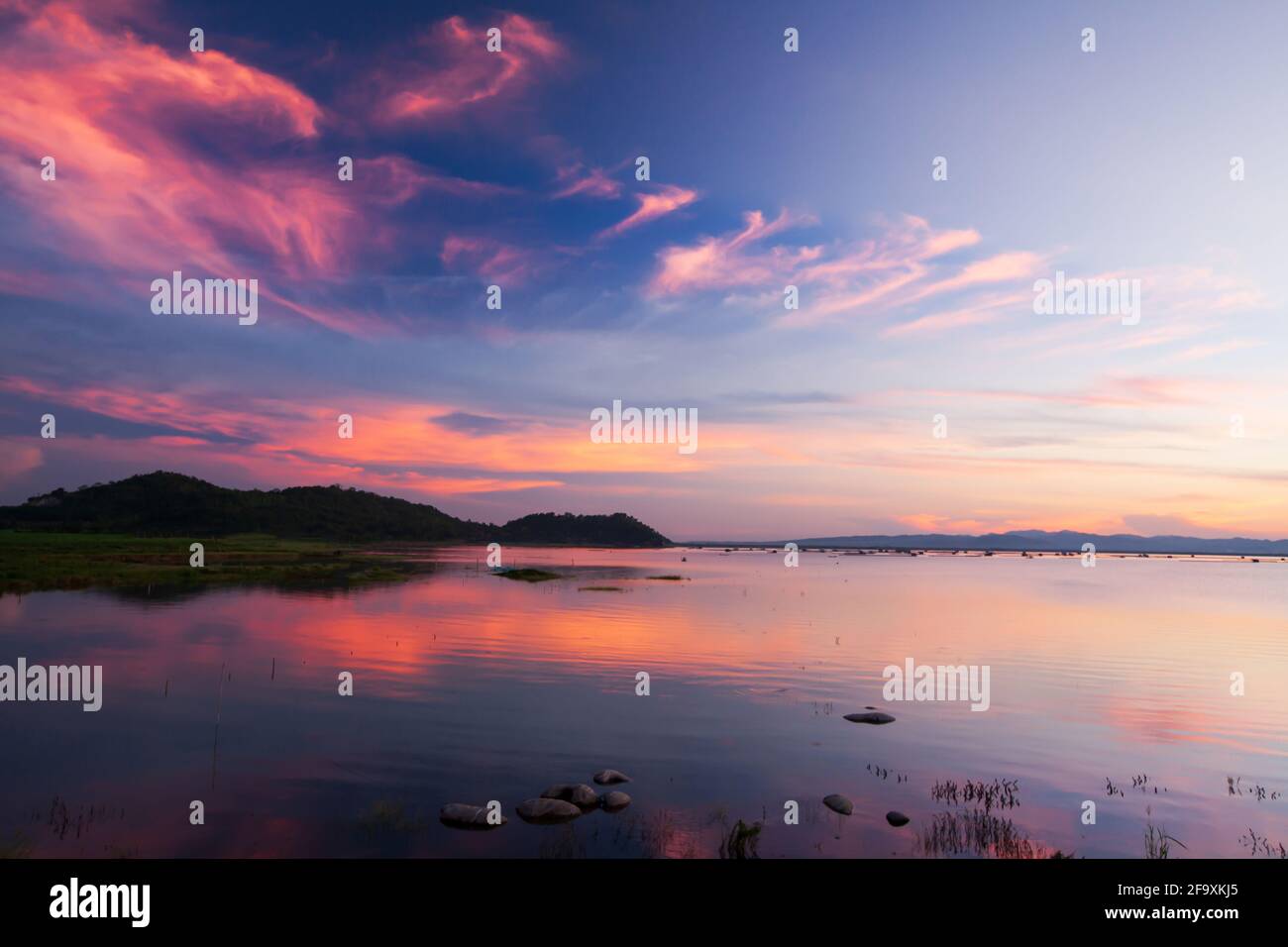 Dramatischer Sonnenuntergang Himmel über einem tropischen See. Wellen rosa Wolken und Sonnenuntergang Himmel Reflexion auf einem See. Westthailand. Stockfoto