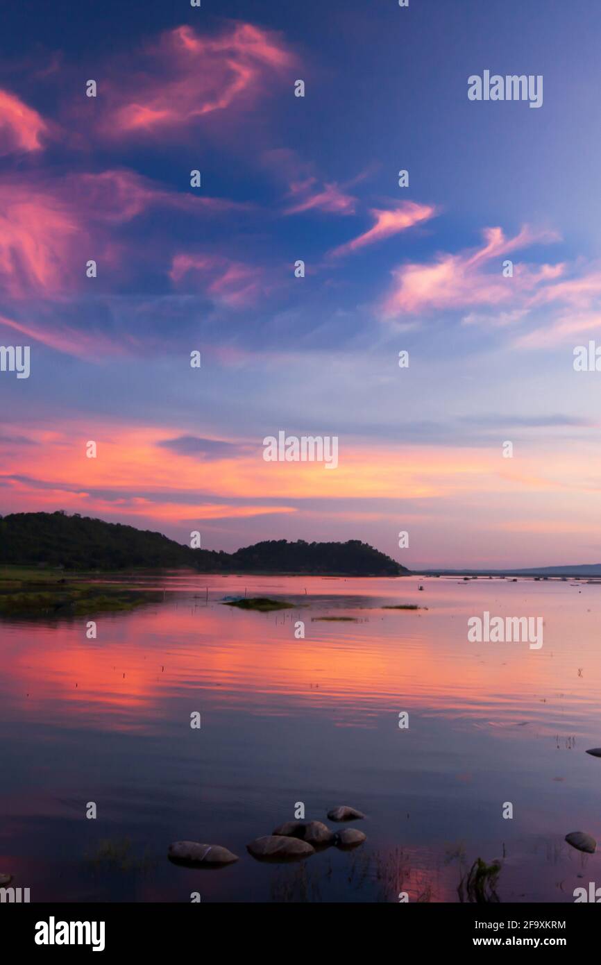 Dramatischer Sonnenuntergang Himmel über einem tropischen See. Wellen rosa Wolken und Sonnenuntergang Himmel Reflexion auf einem See. Westthailand. Stockfoto