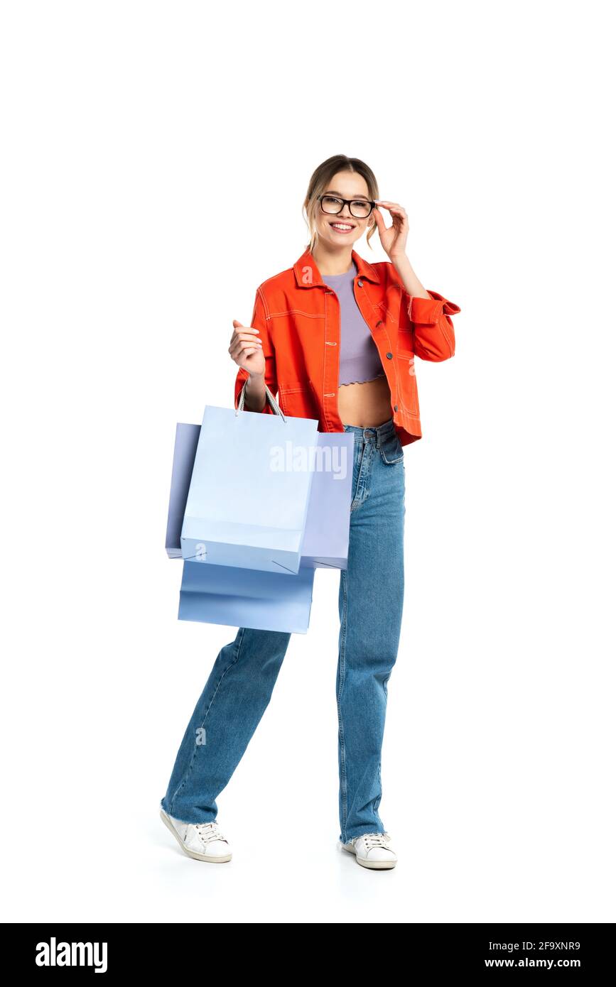 In voller Länge lächelnde Frau in orangefarbenem Hemd mit Einkäufen Beutel isoliert auf weiß Stockfoto