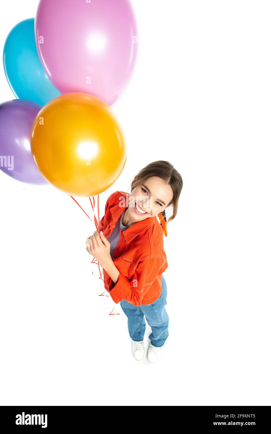 Hochwinkelansicht einer lächelnden jungen Frau in orangefarbenem Hemd Hält bunte Ballons isoliert auf weiß Stockfoto