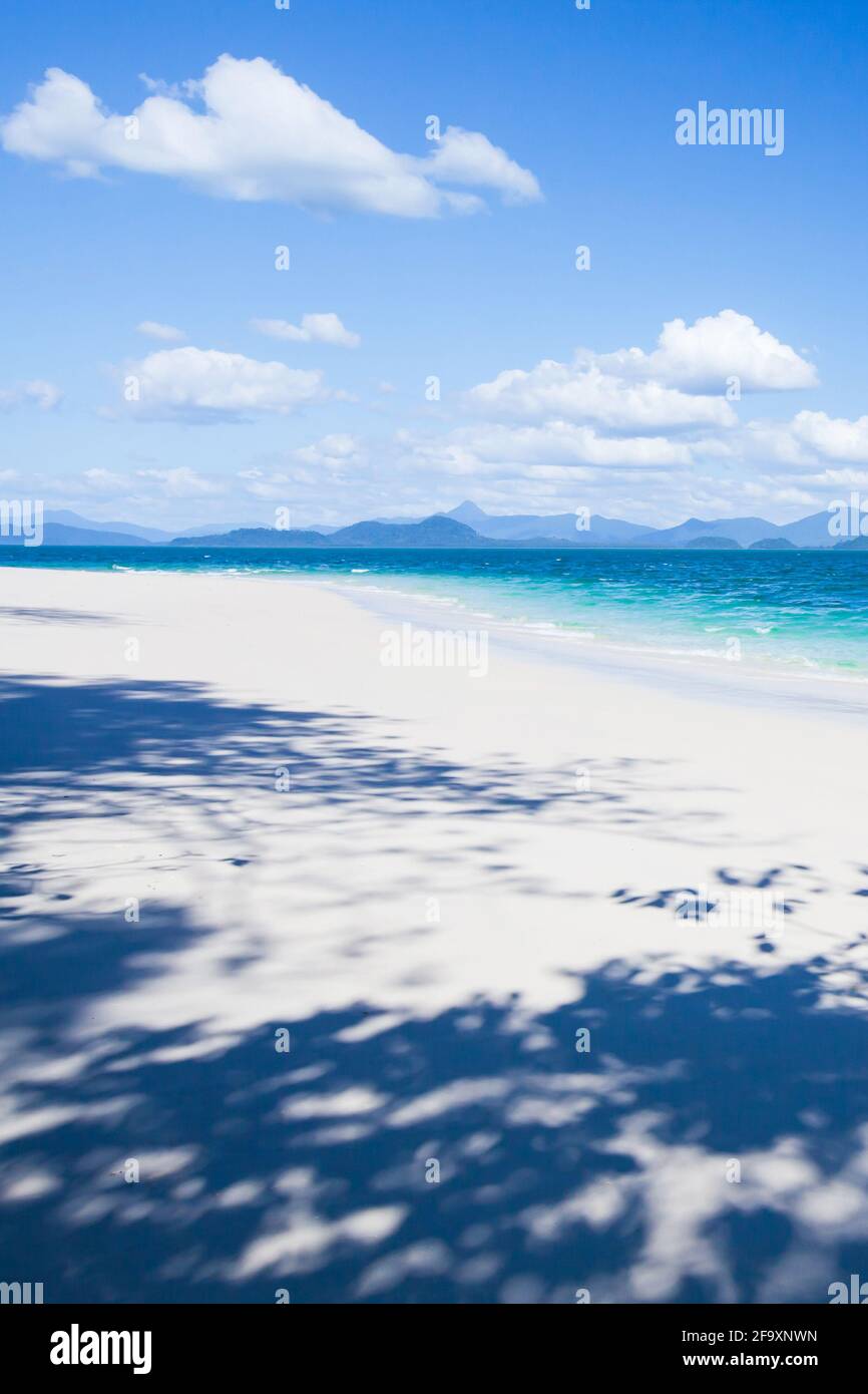 Reine tropische Insel im sonnigen Sommer, strahlend weißer Sandstrand und Wolken gegen blauen Himmel, fantastischer Schatten von Bäumen am Sandstrand. Thailand. Stockfoto