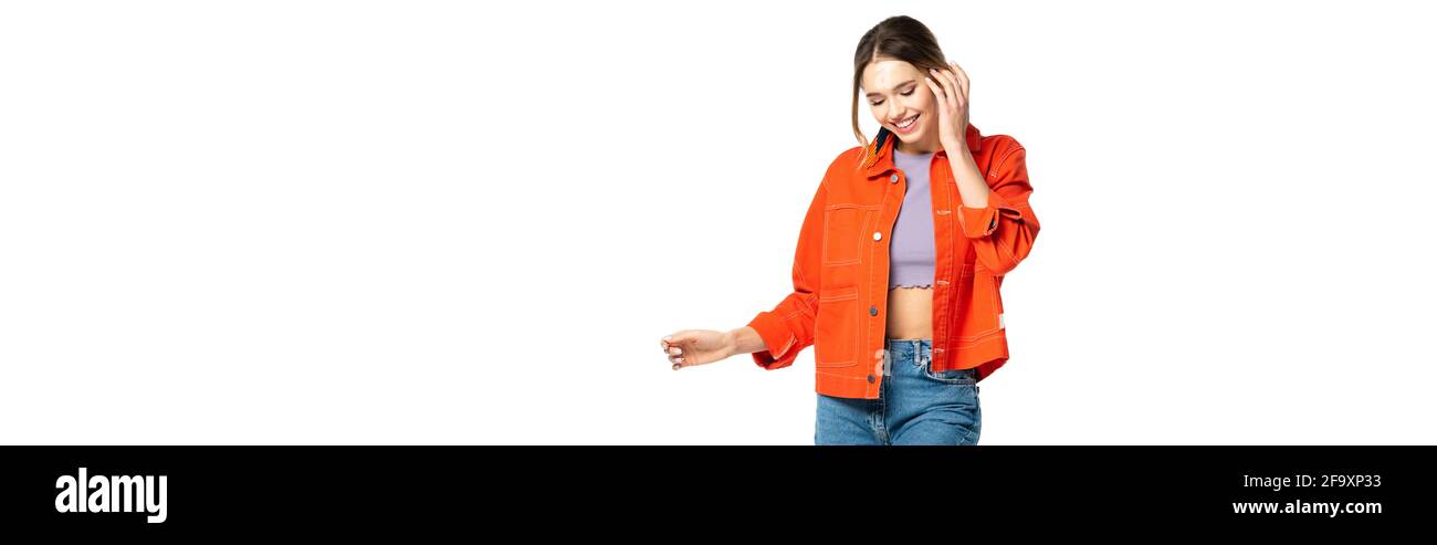 Lächelnde junge Frau in Jeans, Crop Top und orangefarbenem Hemd, isoliert auf weißem Banner Stockfoto