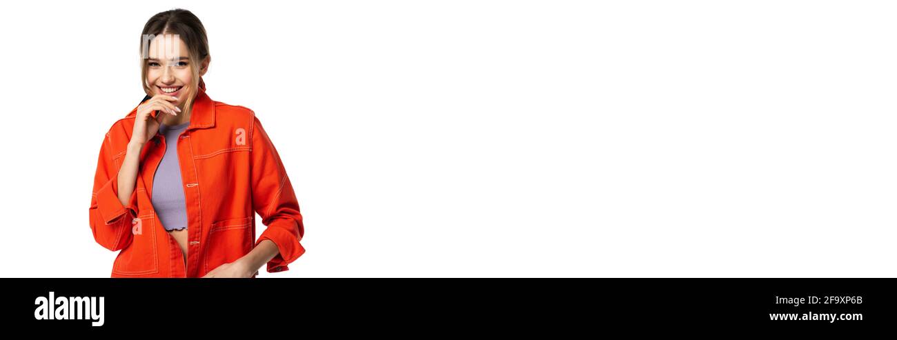 Fröhliche Frau in Crop Top und orangefarbenem Hemd lächelnd isoliert auf weißem Banner Stockfoto