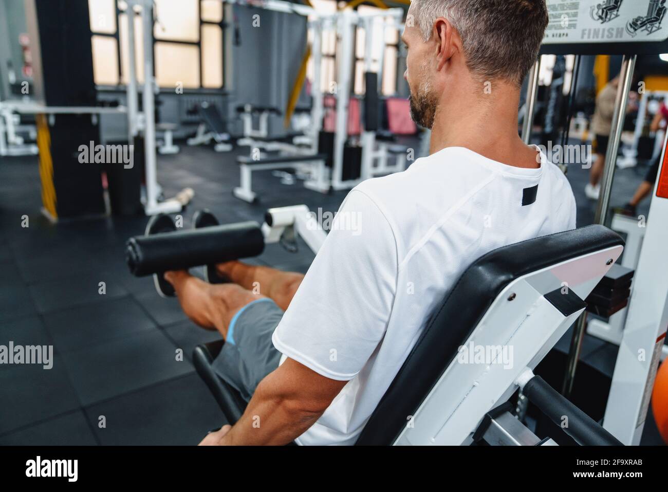 Attraktiver, selbstbewusster, gesunder Sportmann mit sitzender Beincurl-Maschine im Fitnessstudio, Seitenansicht Stockfoto