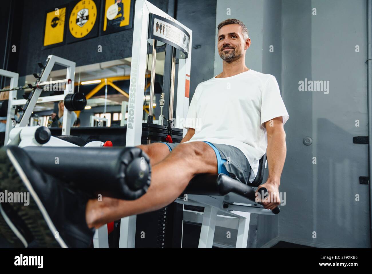 Attraktiver selbstbewusster gesunder Sportmann mit sitzender Beincurl-Maschine Im Fitnessstudio Stockfoto