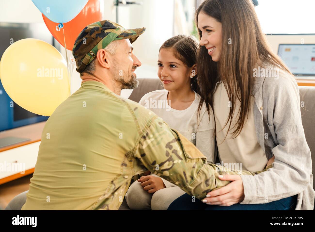 Glückliche Kinder und ihre Mutter treffen Militärpapa in Uniform drinnen. Familienzusammenführung oder Heimkehrkonzept Stockfoto