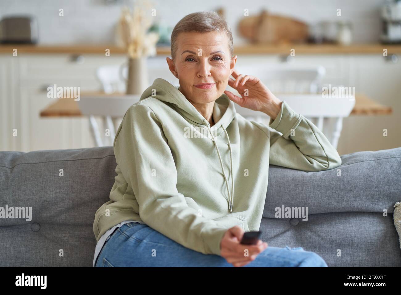 Filmzeit. Porträt einer schönen Frau mittleren Alters mit Fernbedienung in der Hand Fernsehen, während sitzen und entspannen auf dem Sofa, Freizeit zu Hause verbringen. Selektiver Fokus auf ältere Frauen Stockfoto