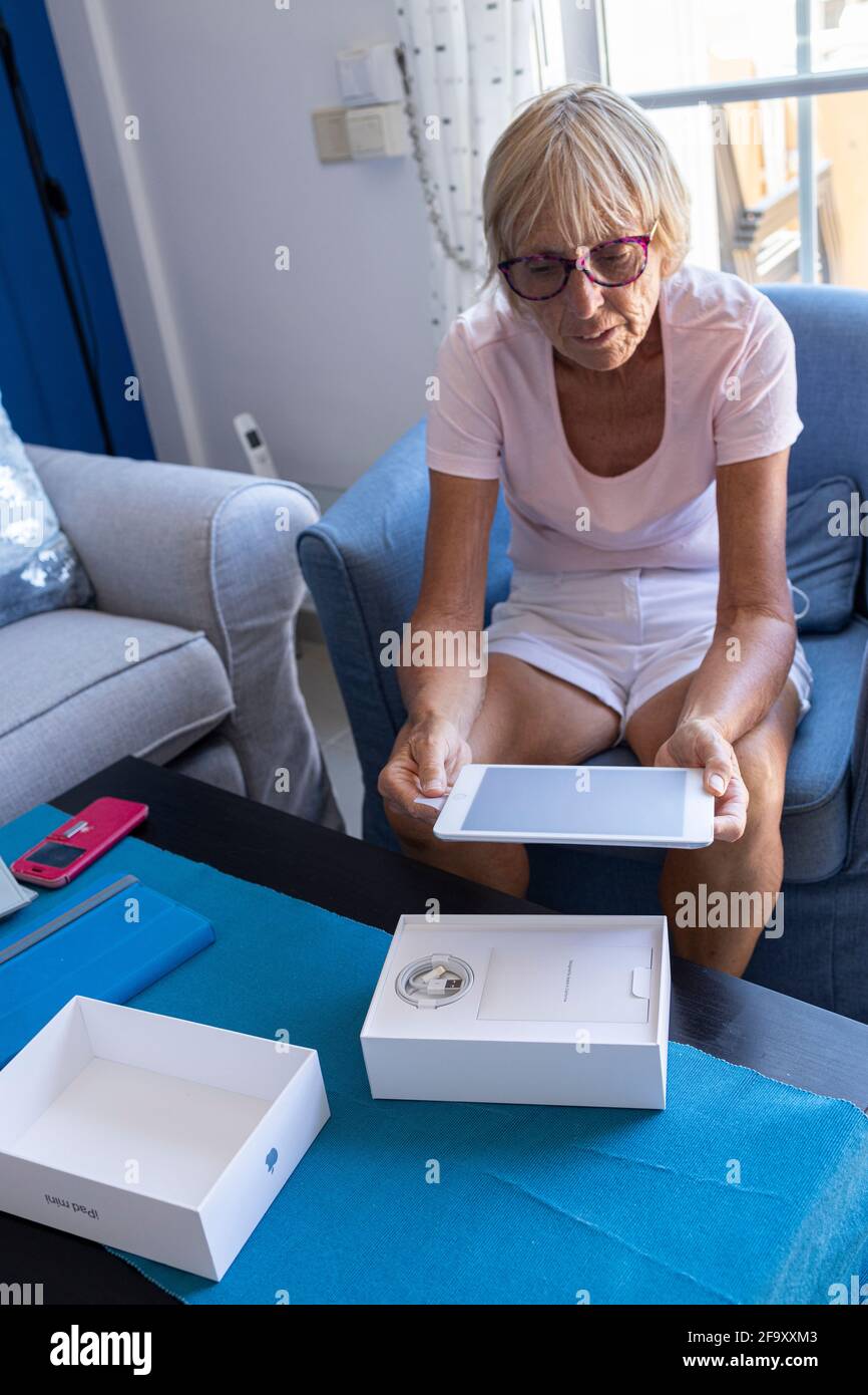 Ältere Frau beim Auspacken eines neuen Apple ipad Mini Tablets in ihrem Wohnzimmer. Stockfoto