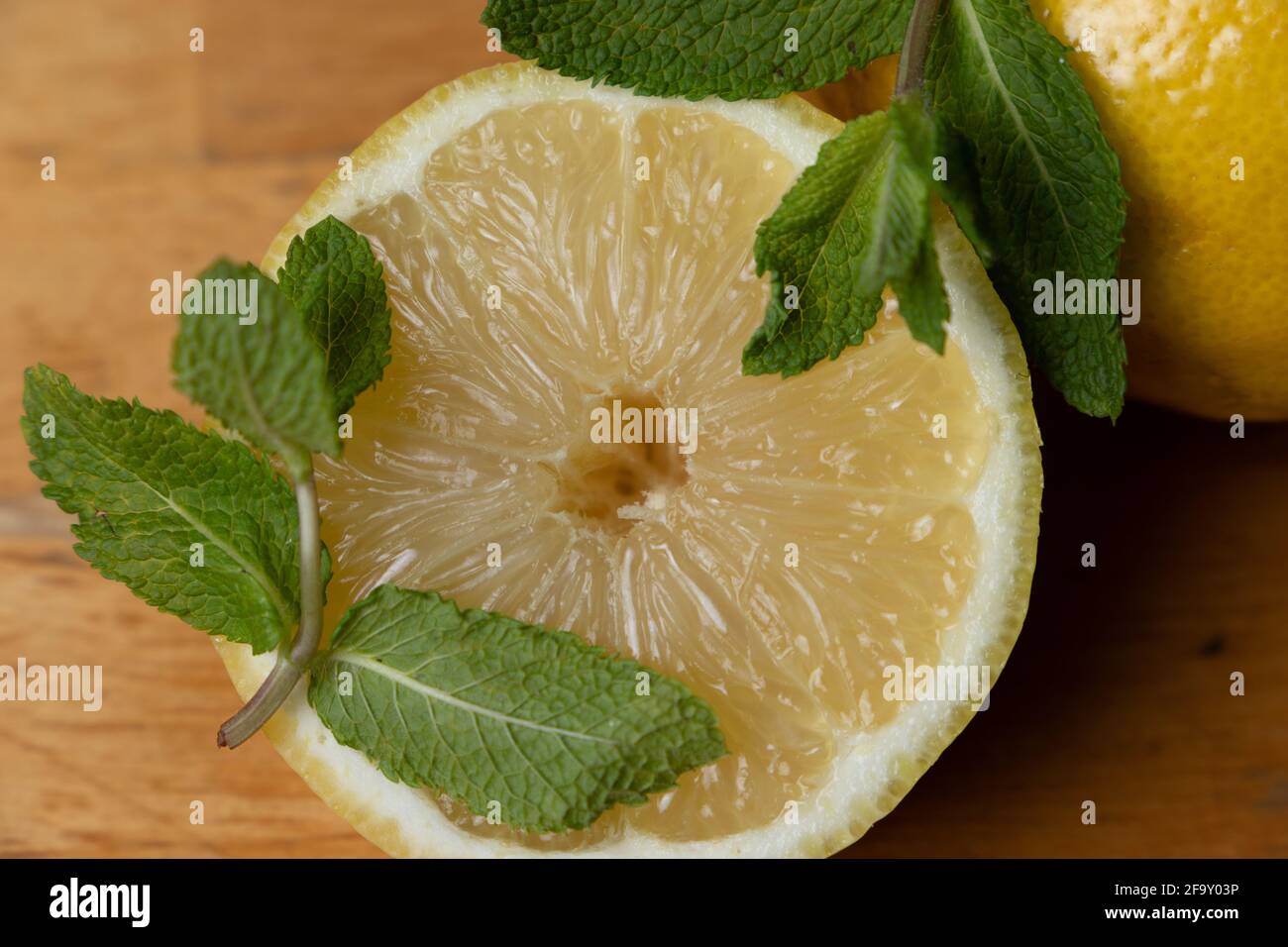 Frische halbe Zitrone mit Minzblättern auf einem Holztisch Stockfoto