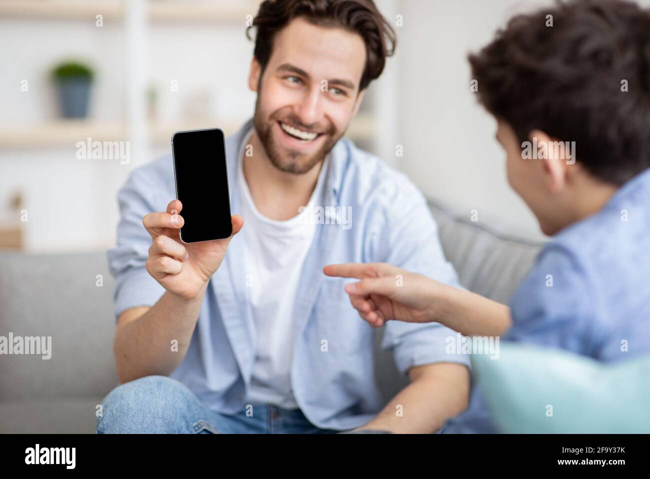 Modernes Technologiekonzept. Vater zeigt seinem Sohn Smartphone mit schwarzem leeren Bildschirm, Telefon mit Platz für Nachbau Stockfoto