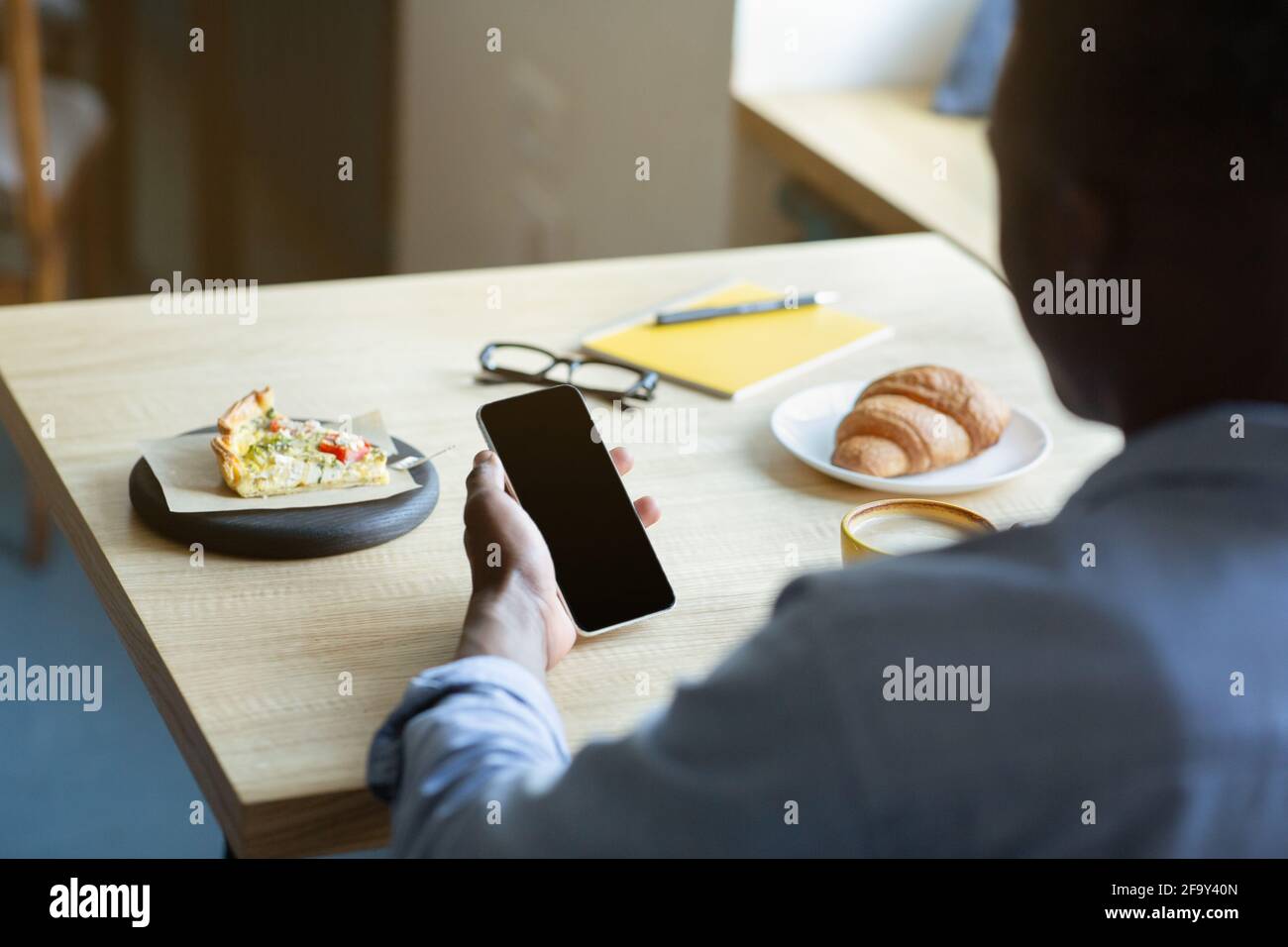 Nahaufnahme eines schwarzen Mannes, der Handy mit leerem Bildschirm hält, während er im Café zu Mittag aß, Modell für mobiles App-Design Stockfoto