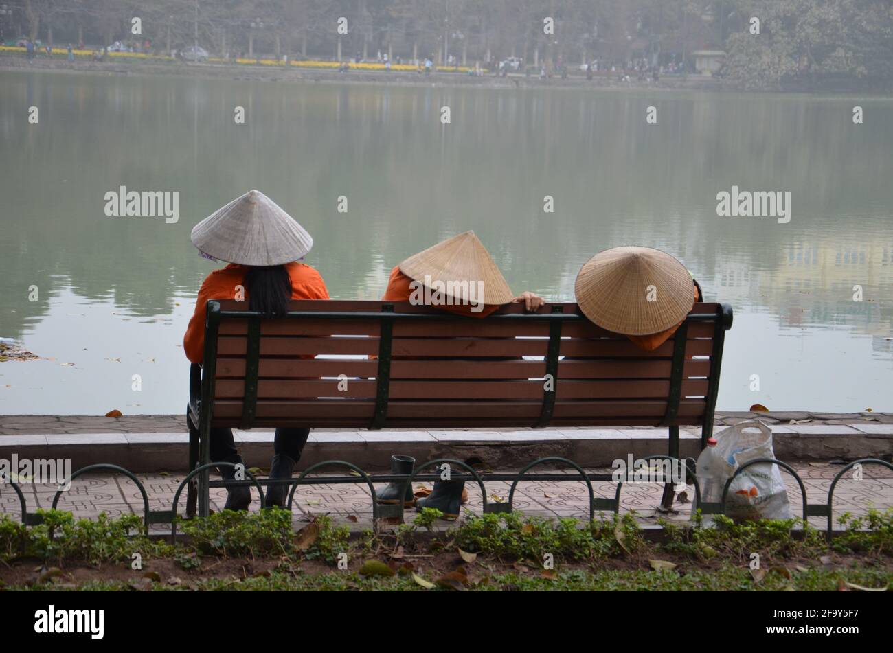 Reflexion von drei Mädchen mit vietnamesischen Hüten über einem nebligen grünen See. Stockfoto